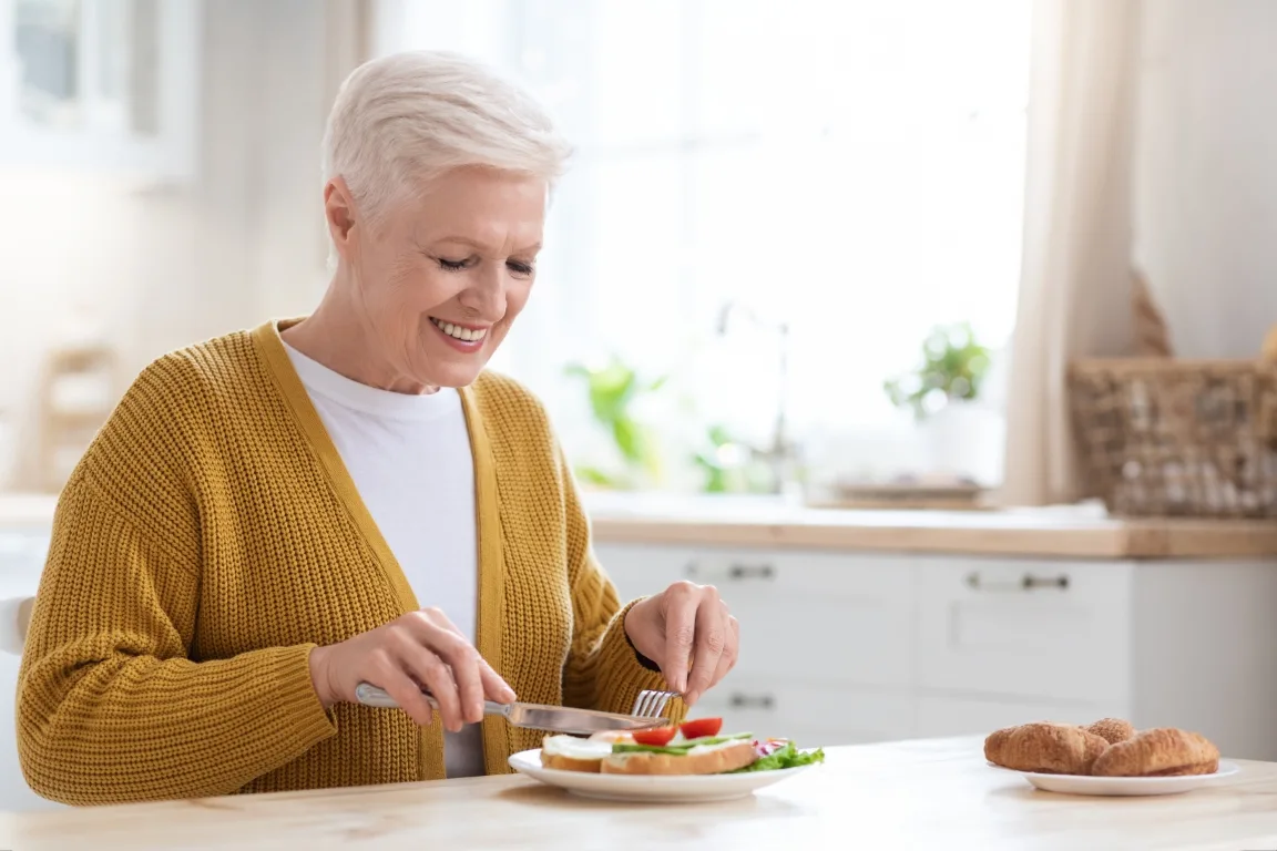 Attractive grandmother having lunch in kitchen alone